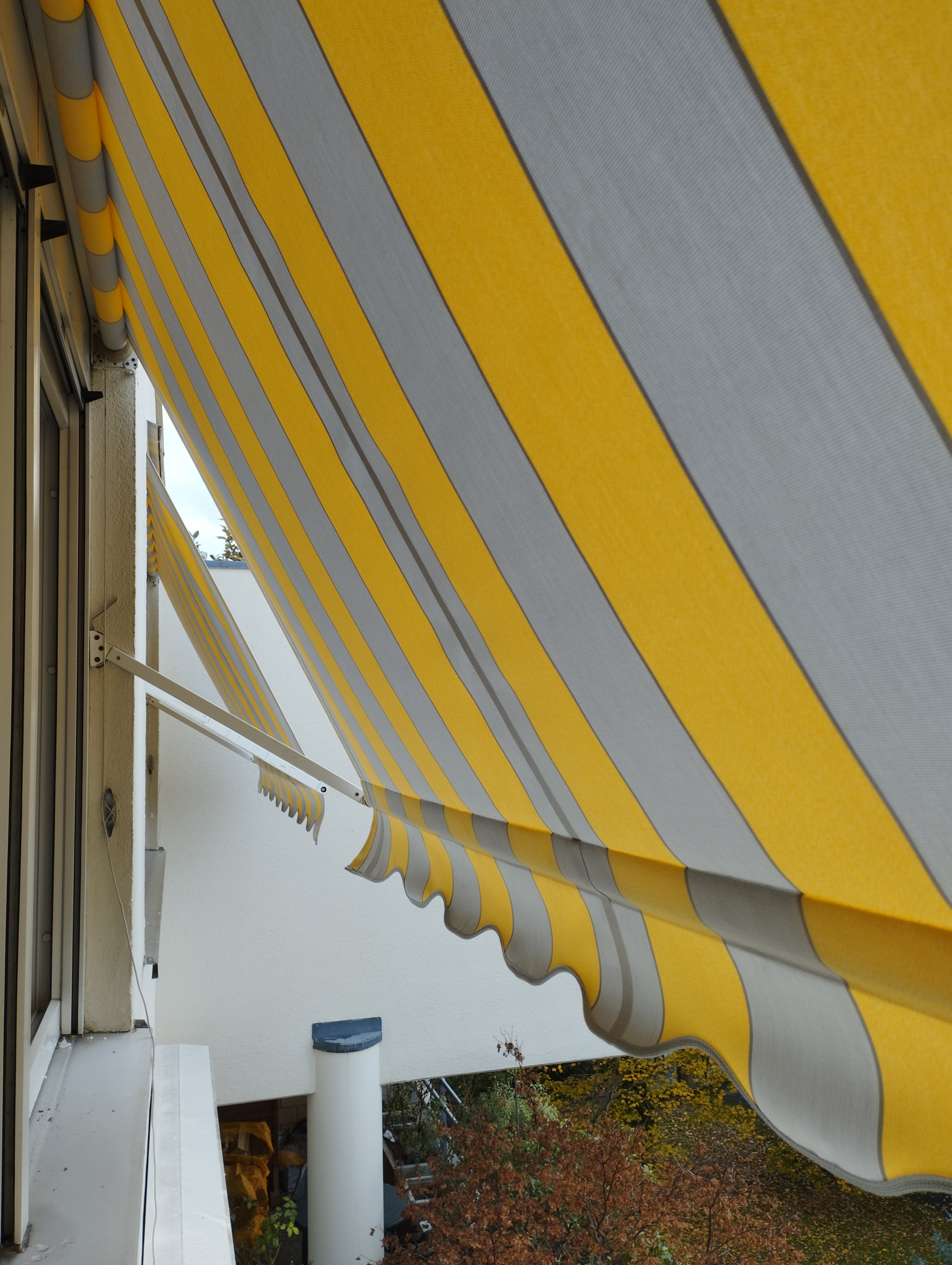 Store banne extérieur rayé jaune et gris déployé sur terrasse, protection solaire efficace à Guebwiller
