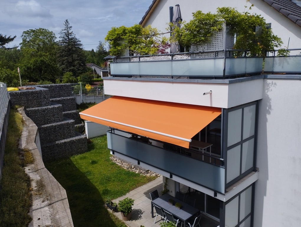 Store banne orange installé sur balcon d’appartement, protection solaire extérieure moderne en Alsace