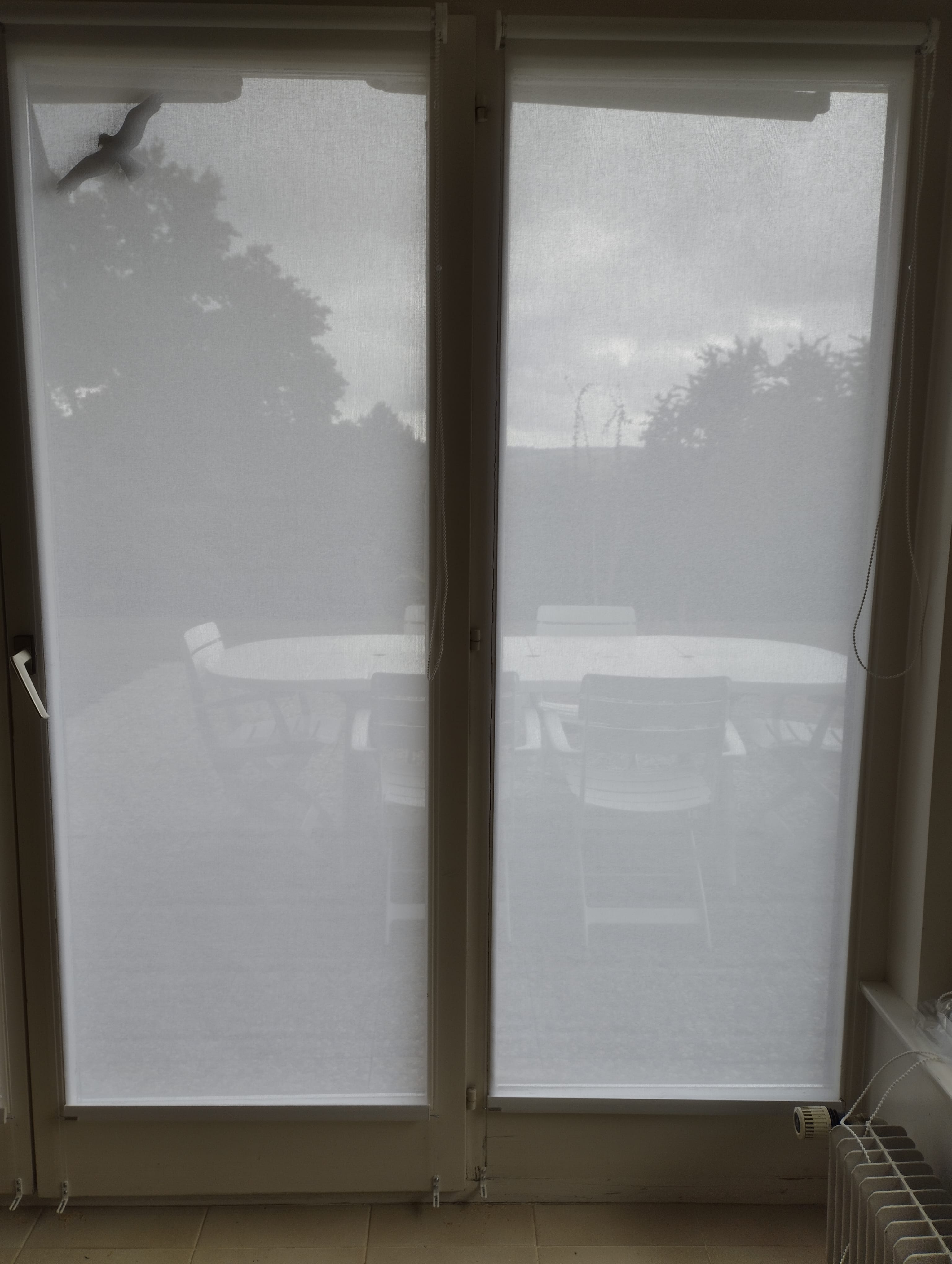 Store intérieur tamisant blanc installé sur une baie vitrée donnant sur une terrasse, filtrant la lumière naturelle