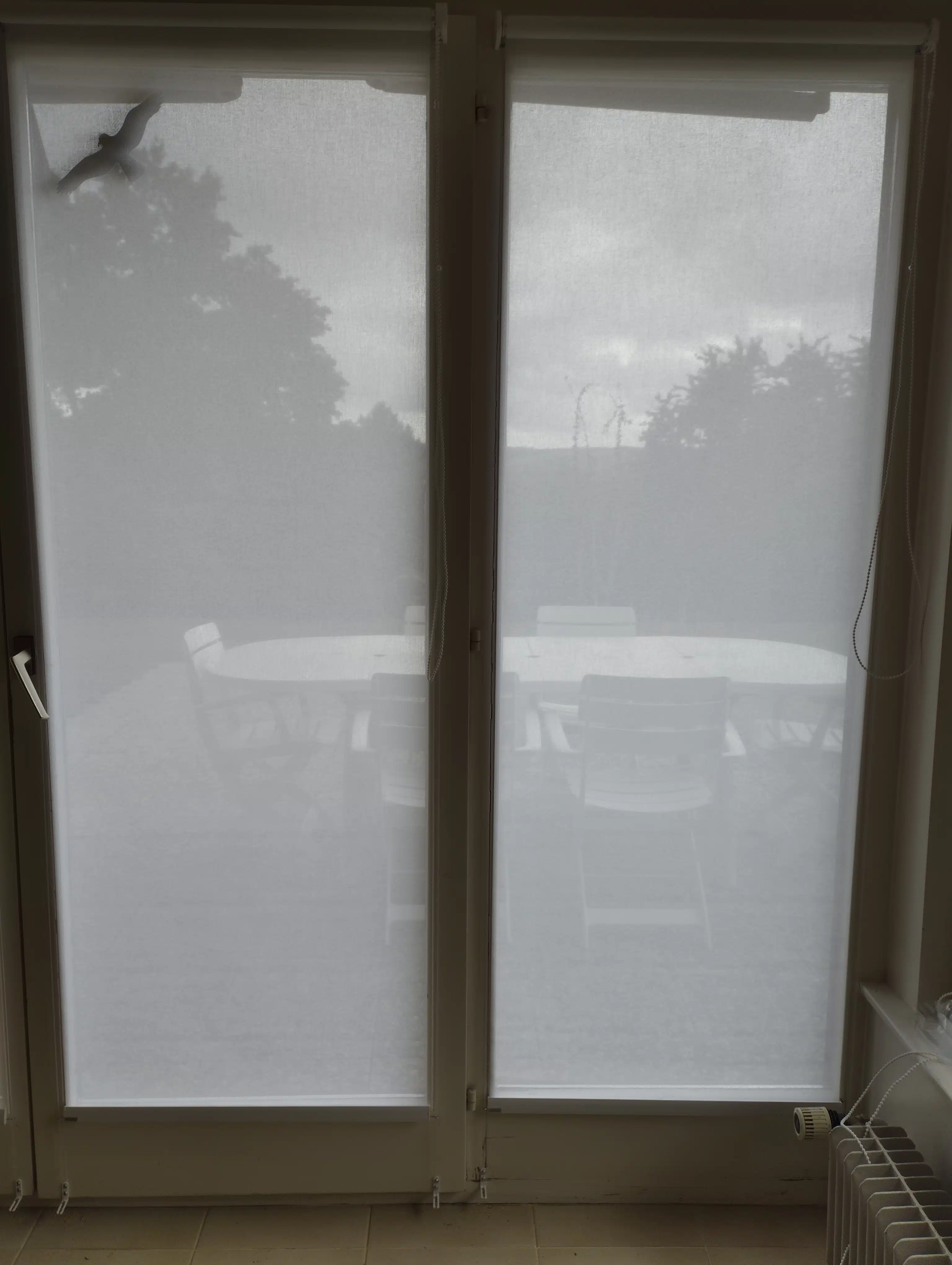 Store intérieur tamisant blanc installé sur une baie vitrée donnant sur une terrasse, filtrant la lumière naturelle